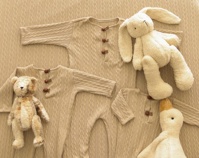 Tres conjuntos de bebé de punto color beige con botones, dispuestos sobre un fondo blanco.