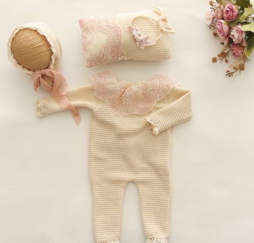 Conjunto de punto color crema para bebé con gorro rosa, zapatitos y flores sobre un fondo beige suave.
