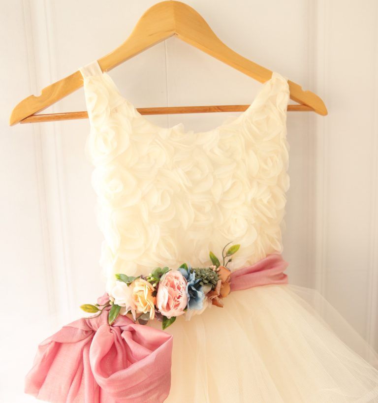Tres trajes de ballet de tul blanco en perchas de madera, uno con cintas y flores rosas.