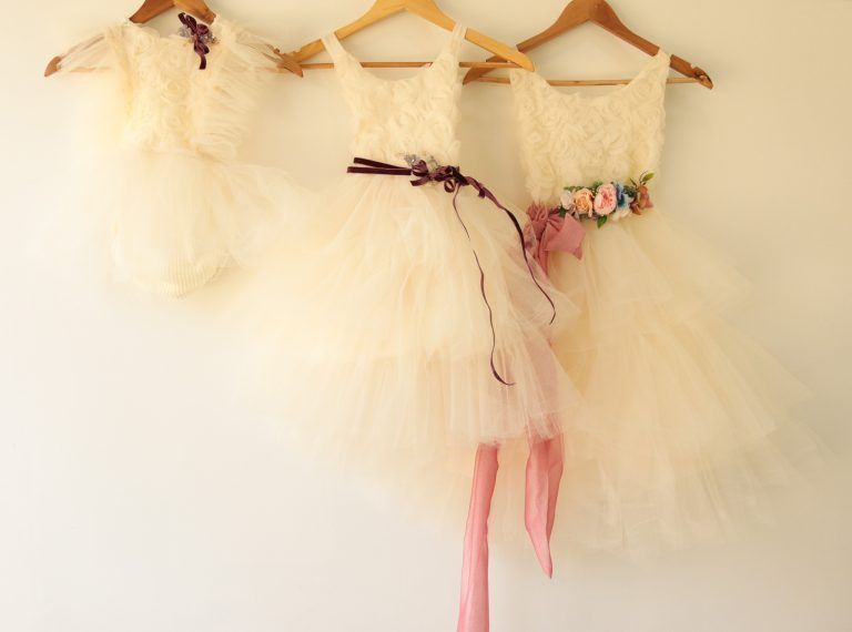 Tres trajes de ballet de tul blanco en perchas de madera, uno con cintas y flores rosas.