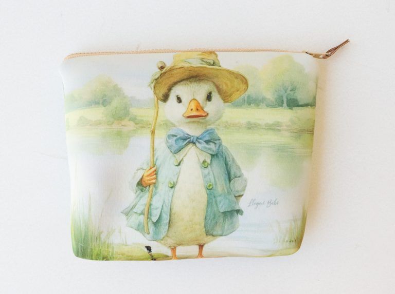 Bonita ilustración de un pato en una camiseta color crema, con estampados de patos a juego en tarjetas cercanas.