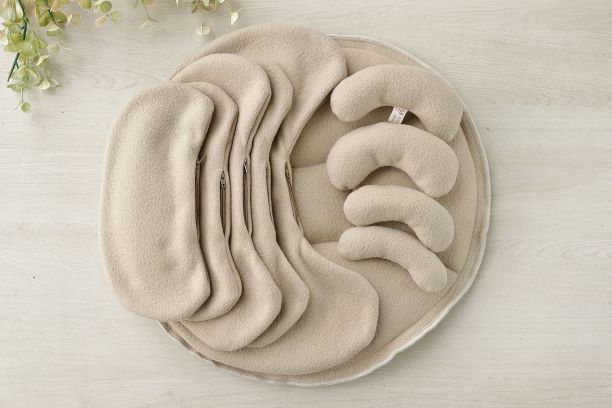 Tela beige doblada, dispuesta en capas con formas circulares y de media luna sobre una superficie de madera clara.