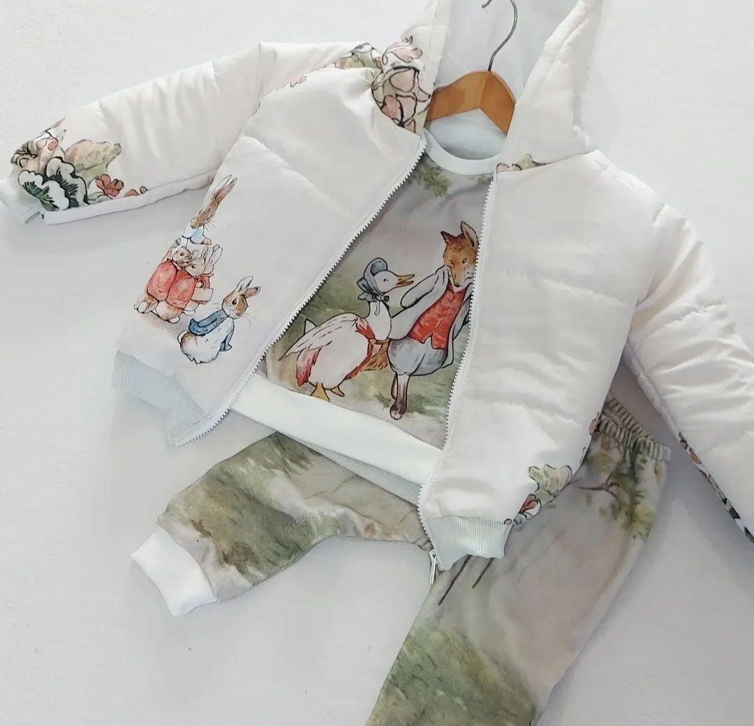 Chaqueta y pantalón acolchados blancos para bebé con estampado animal en tonos pastel, colgados en una percha.