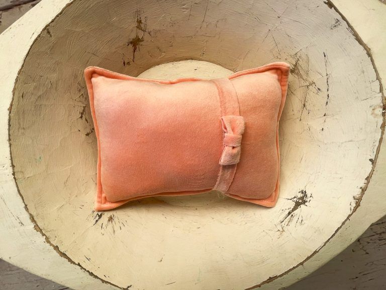 Cinco bolsitas de tela en tonos pastel alineadas en una bandeja rústica de madera sobre un fondo blanqueado.