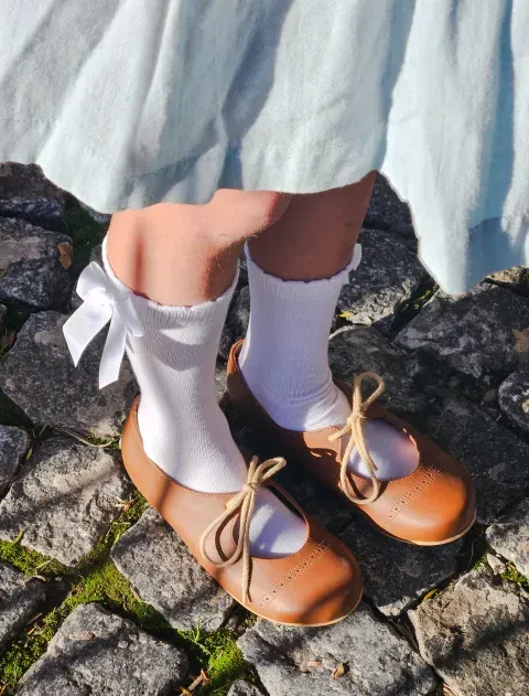 Calcetines blancos y zapatos marrones con lazo sobre adoquines bajo una falda azul claro