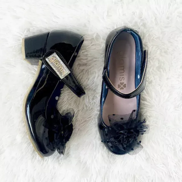 Zapatos de tacón alto de encaje negro con lazos, presentados sobre una tela de encaje negro transparente.