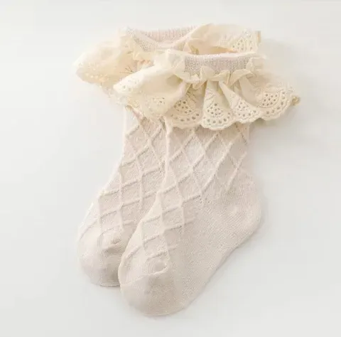 Calcetín rosa de bebé con puño de volantes de encaje color crema sobre fondo blanco.