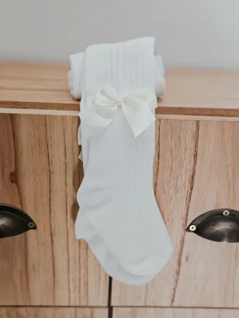 Calcetín blanco de bebé con un lazo colgando de la manija de un armario de madera.