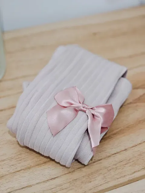 Dos personas con vestidos color crema y marrón, de pie una al lado de la otra y con medias sobre una alfombra.