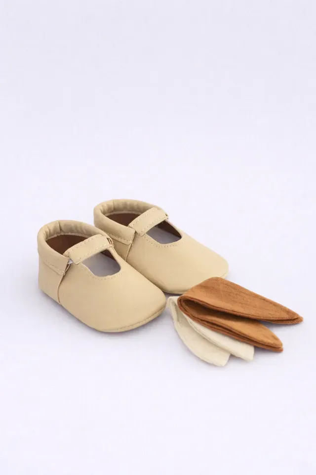 Zapatos de bebé color beige con punteras intercambiables blancas y marrones sobre fondo blanco.
