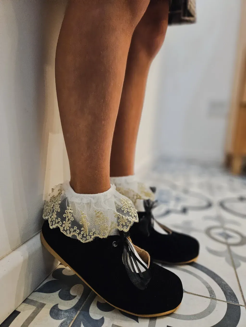 Una zapatilla de ballet sobre un pie elevado, atada con una cinta blanca, sobre un suelo estampado.
