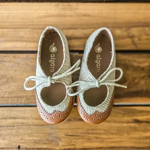 Zapatos marrones con cordones y pantalones a rayas crema y negras sobre un asiento de silla de mimbre.