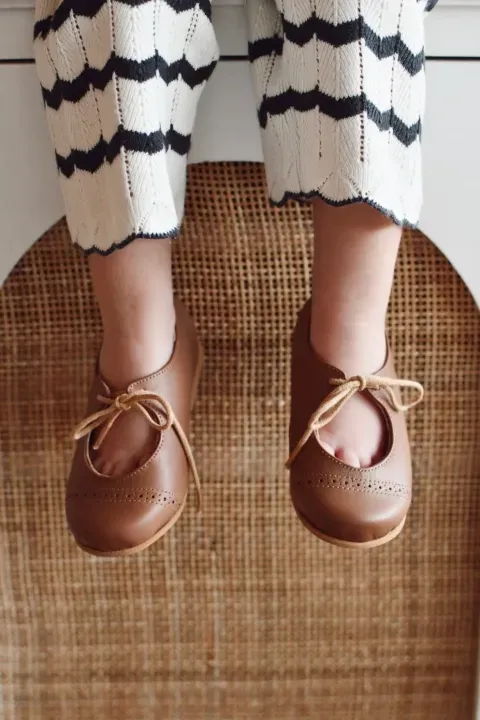 Zapatos marrones con cordones y pantalones a rayas crema y negras sobre un asiento de silla de mimbre.