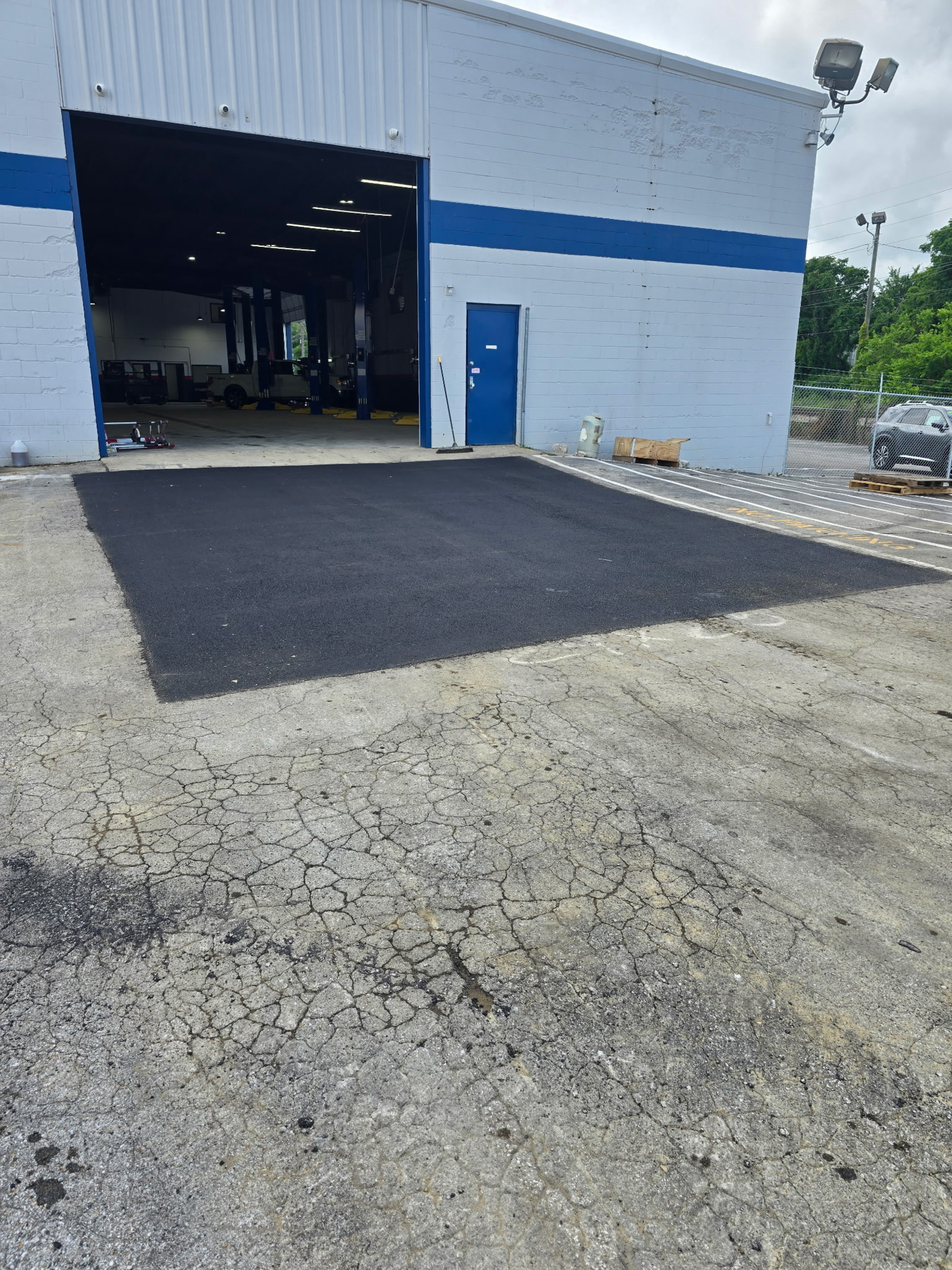 New asphalt area in front of a garage, with a blue door. Gray gravel surrounds.