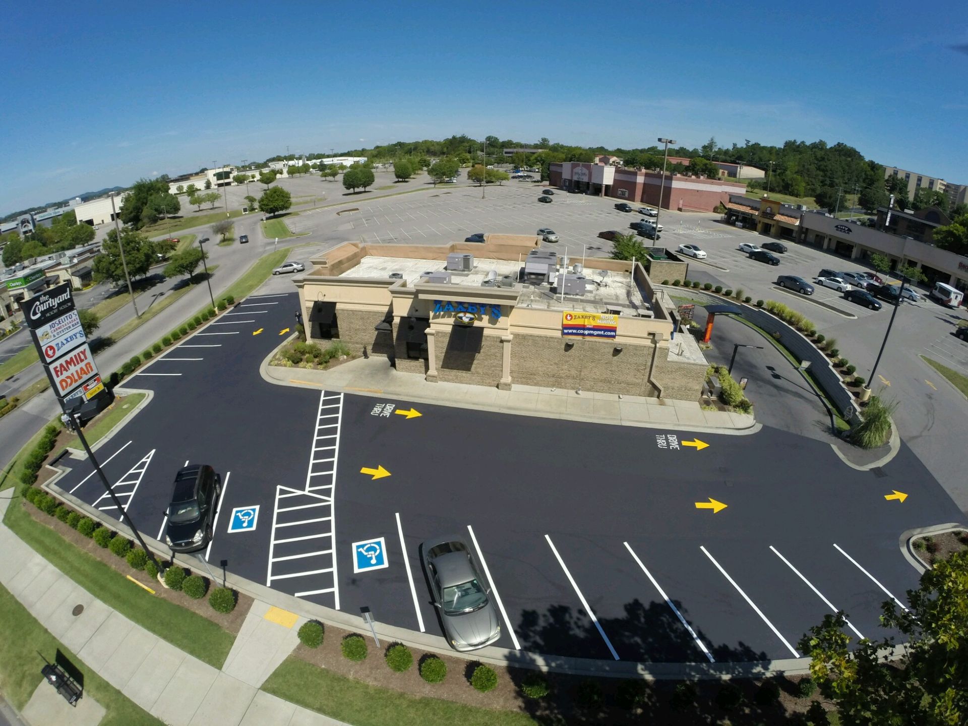 Aerial view of a church with a parking lot. White building with dark roof, surrounded by asphalt and green lawn.