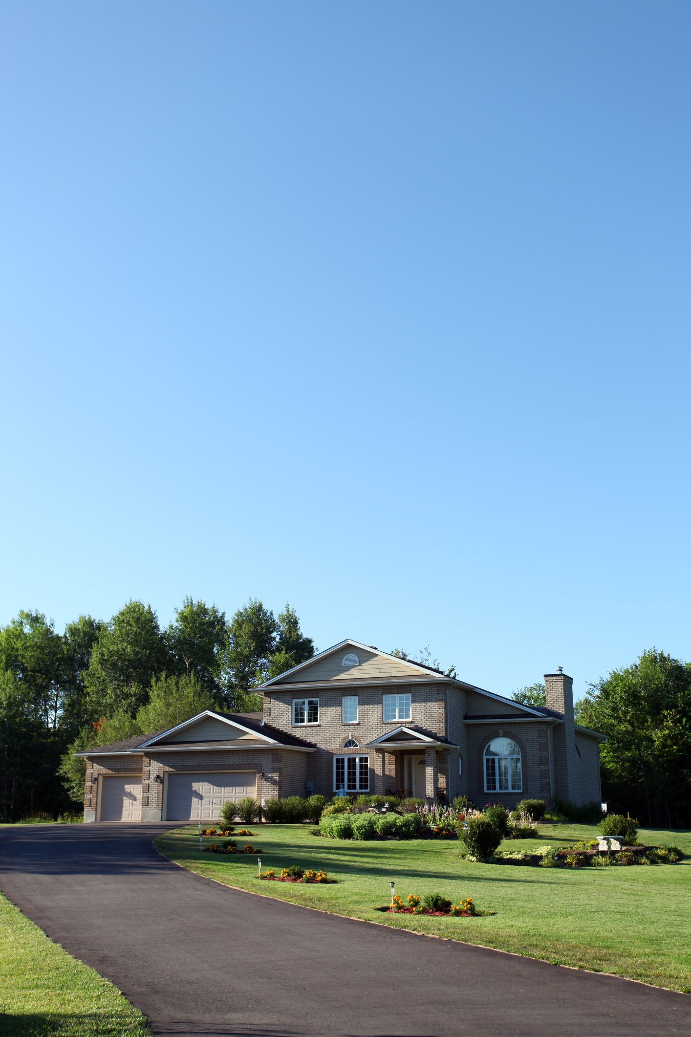 Large stone house with a driveway and attached garage on a sunny day.