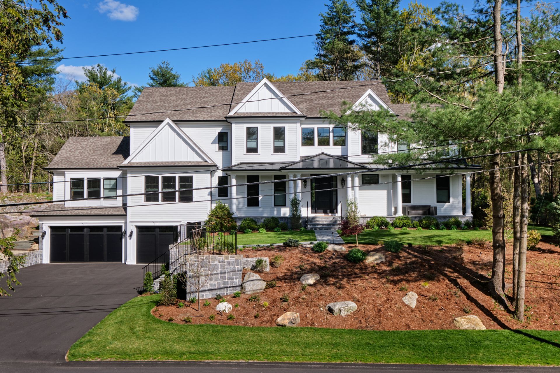 White two-story house with black trim, a driveway, and a well-landscaped yard with trees.