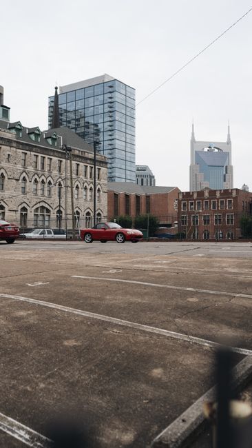 Urban square with a red car, historic buildings, and a modern glass tower under a gray sky