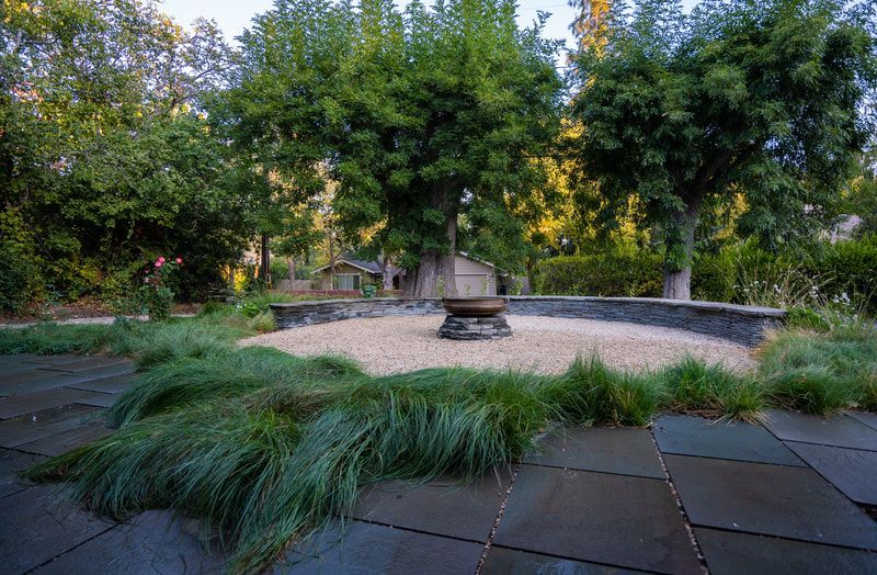 There is a fire pit in the middle of the garden surrounded by trees.