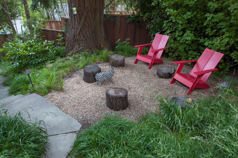 Two red chairs are sitting in a yard next to a tree.