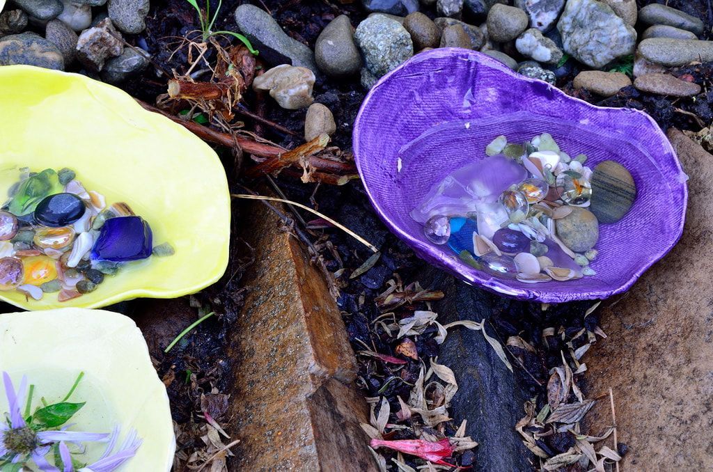 Three bowls filled with rocks and flowers are sitting on the ground.