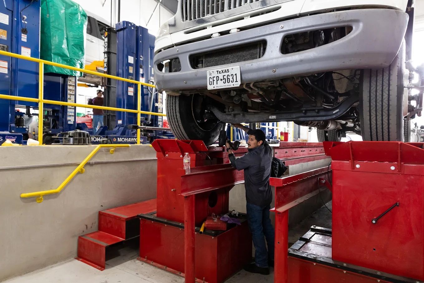 Mechanic inspecting a car raised on a red hydraulic lift in an auto repair shop