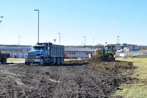 Blue dump truck and bulldozer moving dirt at a construction site on a sunny day.
