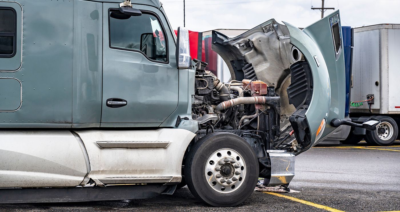 Damaged semi-truck with open hood after collision, parked on a road beside another truck