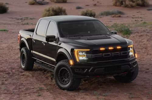 Black off-road pickup truck on a desert trail, front view with amber lights on and oversized tires