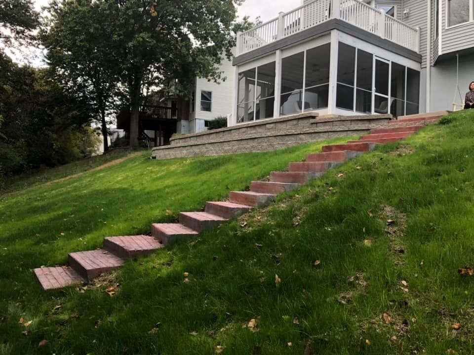Brick steps ascend a grassy hill to a screened porch attached to a white house.
