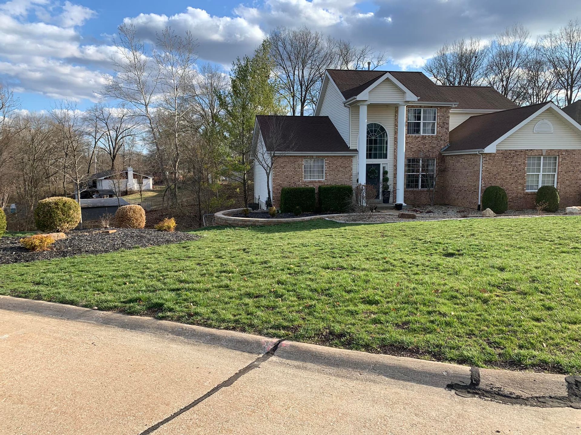 A two-story brick house with a well-kept lawn, under a partly cloudy sky.