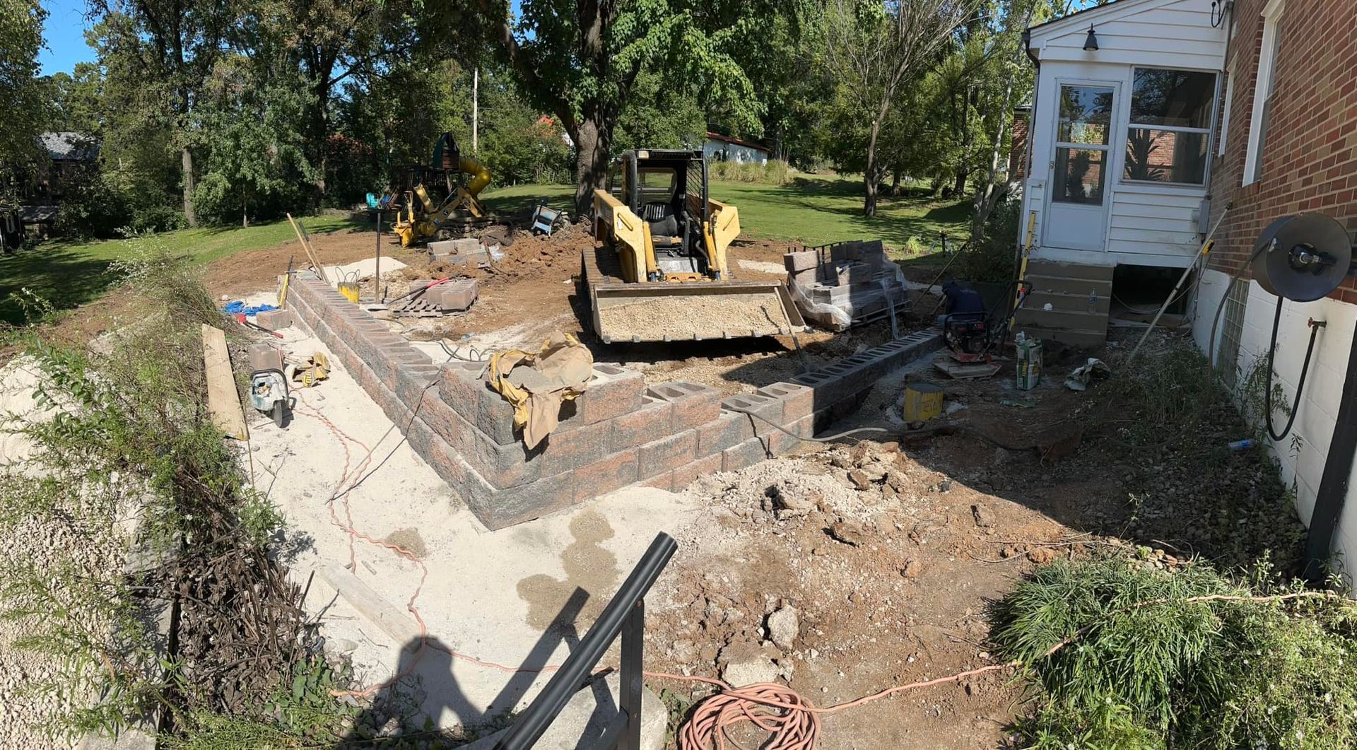 Construction site with a yellow bulldozer, brick foundation, and a house.