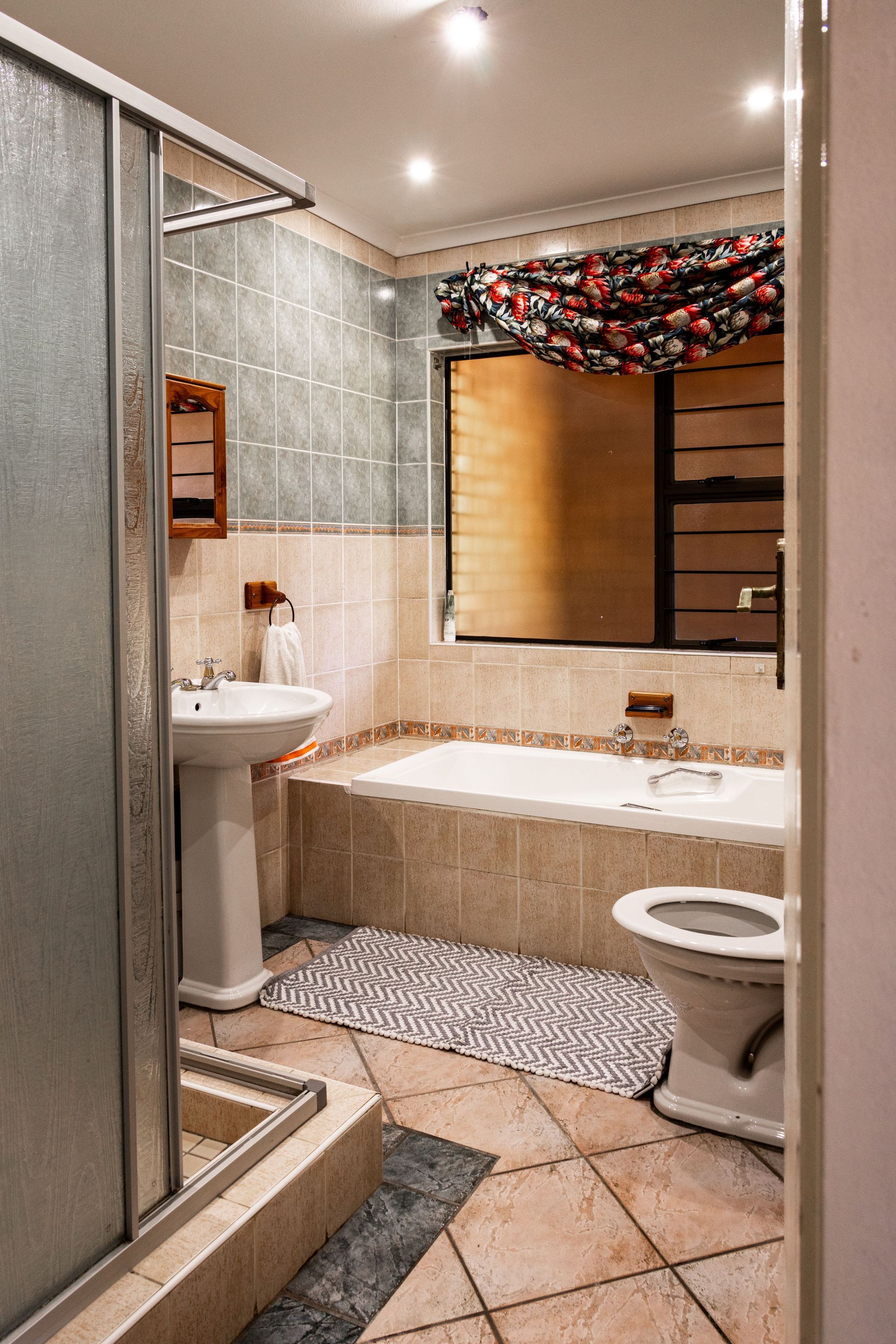Small tiled bathroom with shower, sink, toilet, and a bathtub under a decorated window.