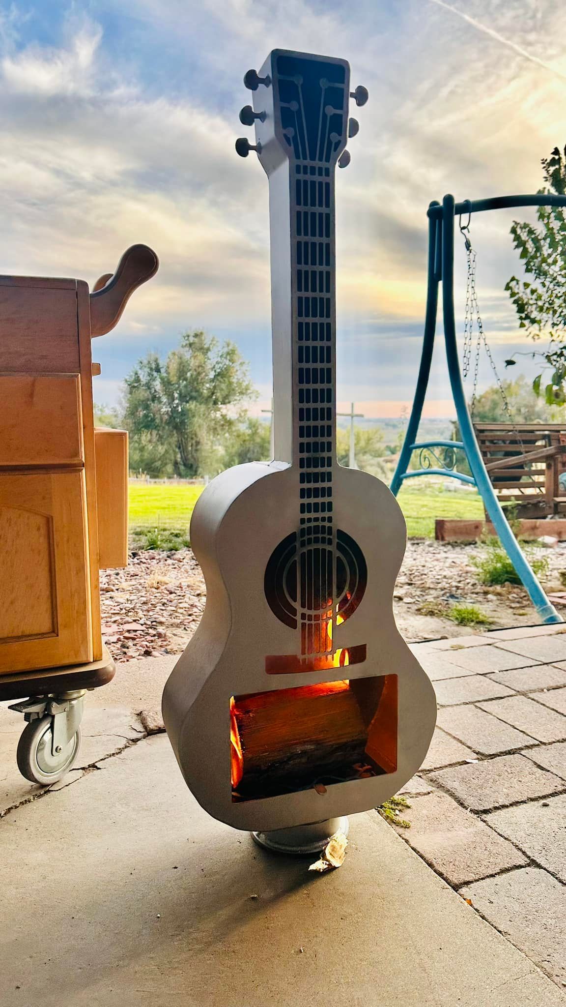 A guitar shaped fireplace is sitting on a patio next to a swing set.