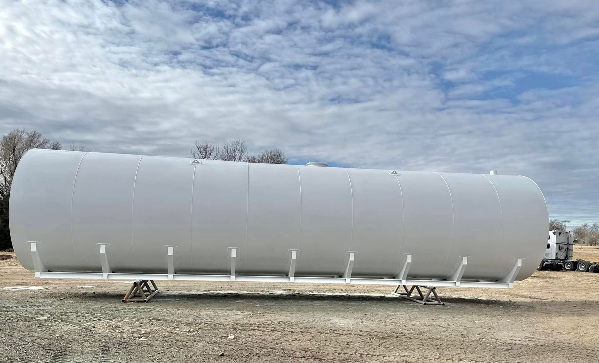 A large white tank is sitting on top of a dirt field.