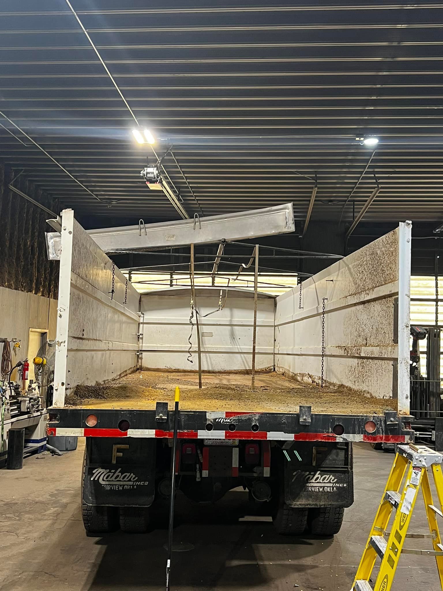 A dump truck is parked in a garage with a ladder in front of it.