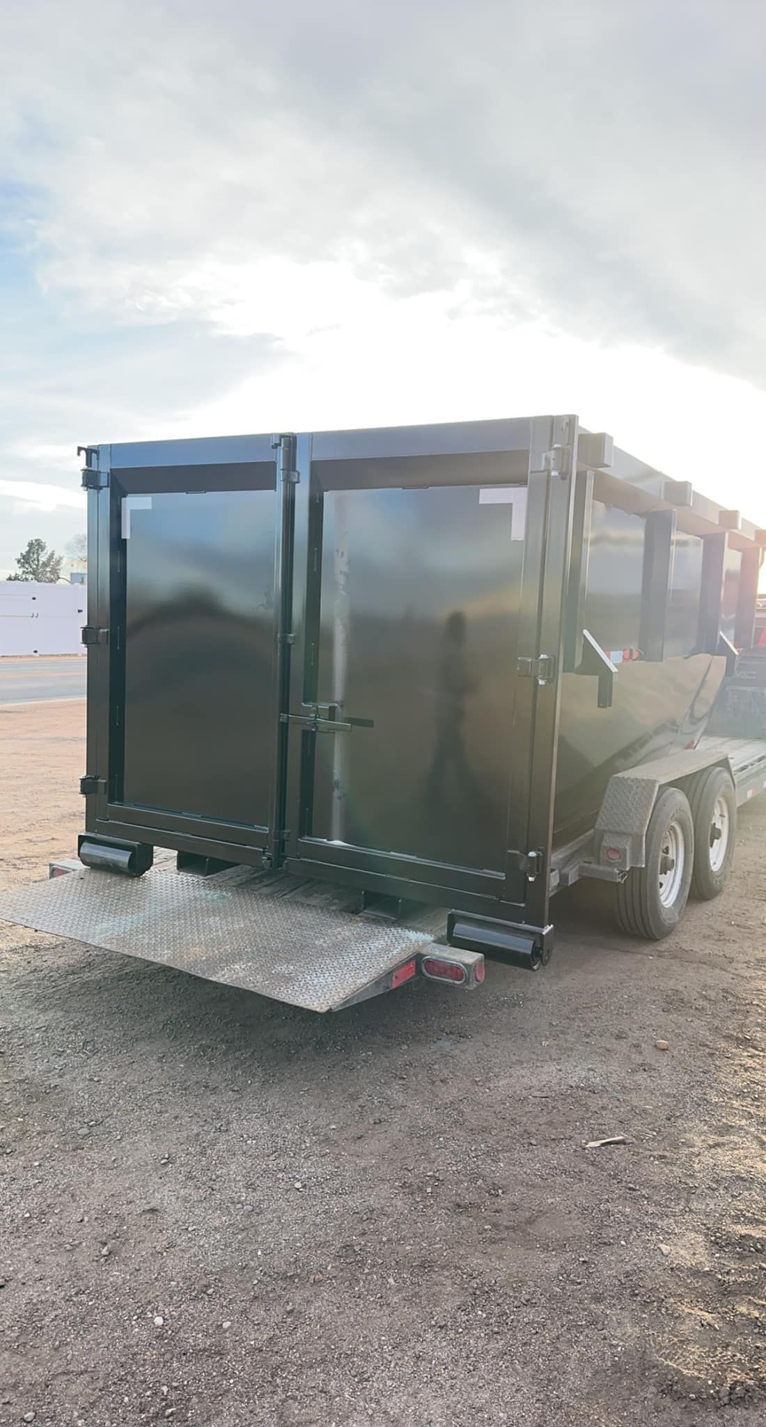A dumpster trailer is parked in a gravel lot.