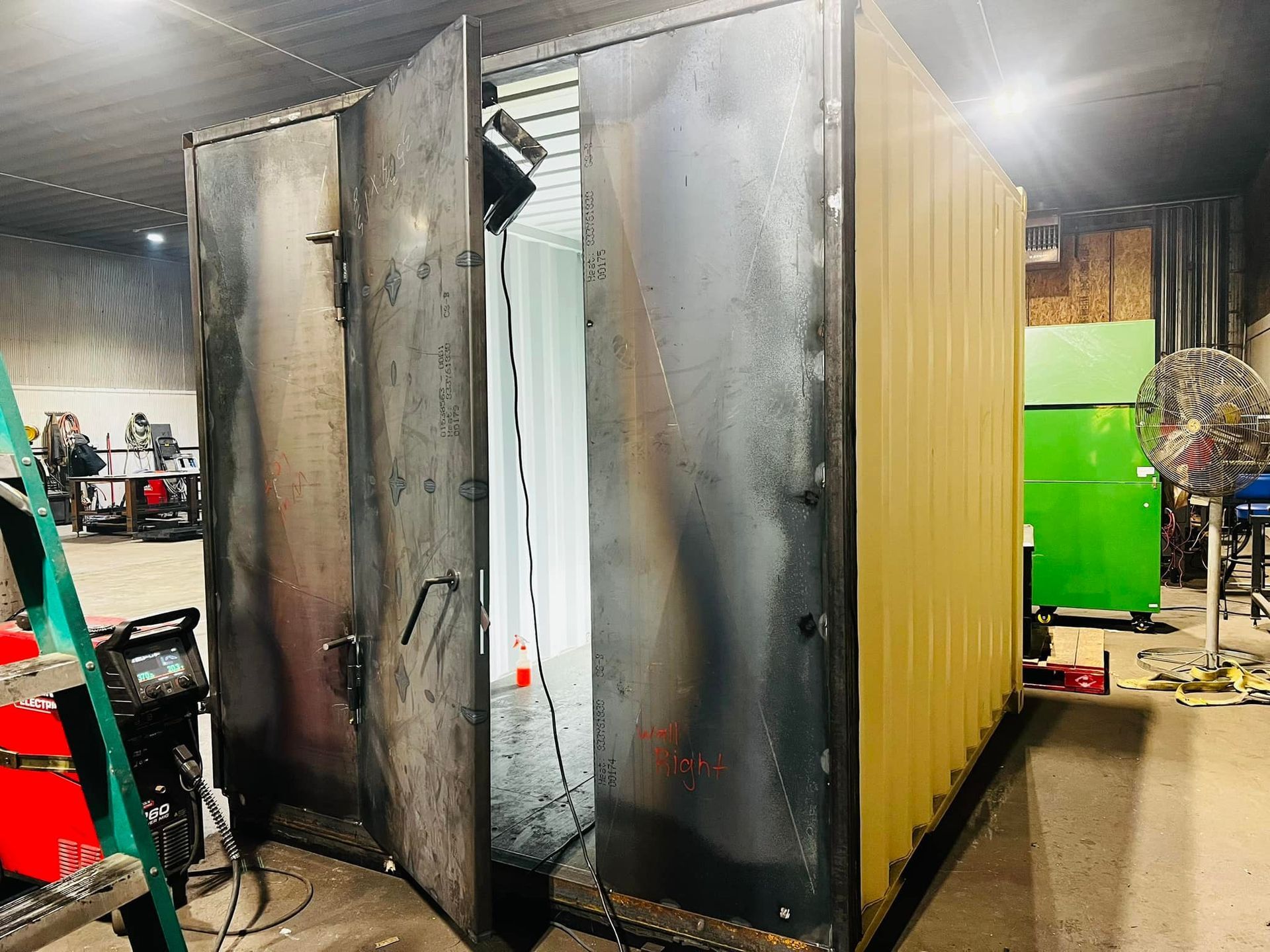 A large metal container is sitting in a warehouse with its doors open.