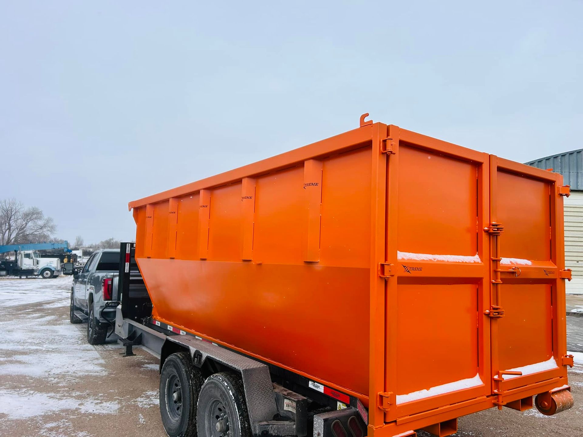 A large orange dumpster is parked next to a truck in a snowy parking lot.