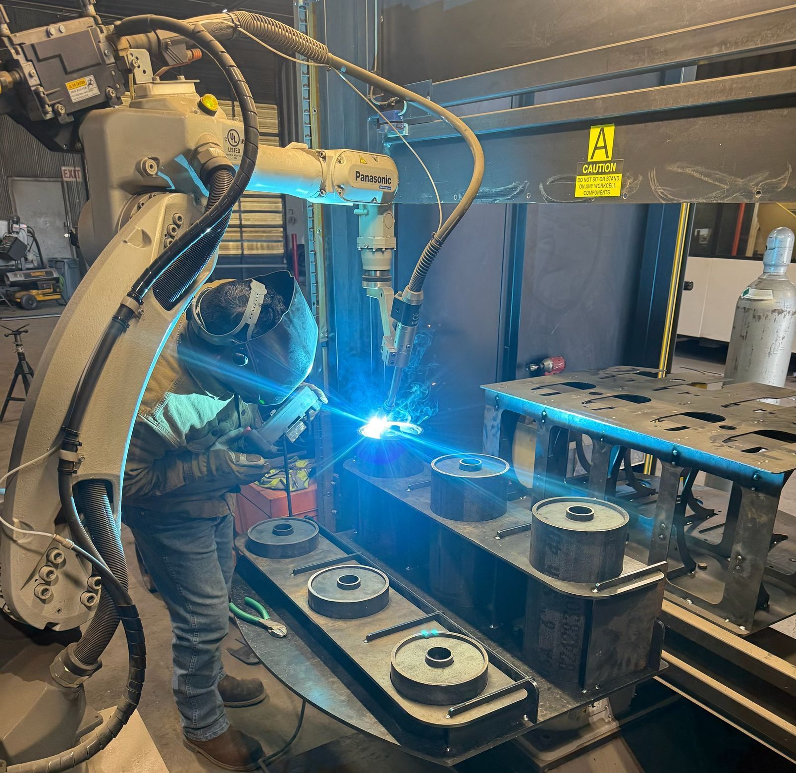 A man is welding a piece of metal with a robotic arm.