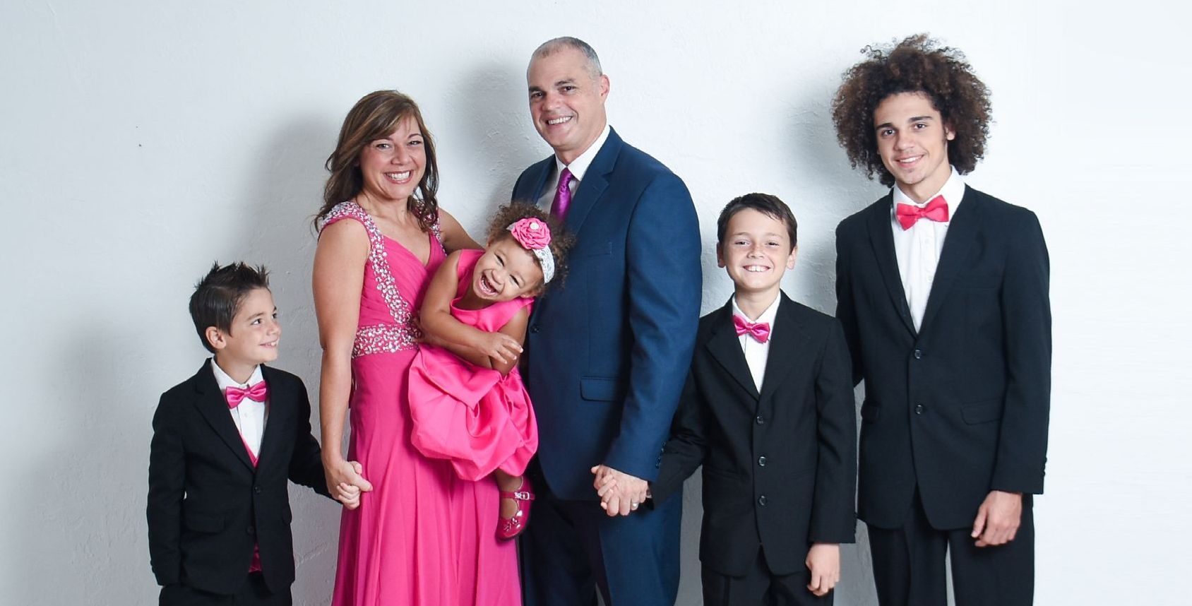 Family of five, dressed in formal attire, poses in front of a white backdrop.