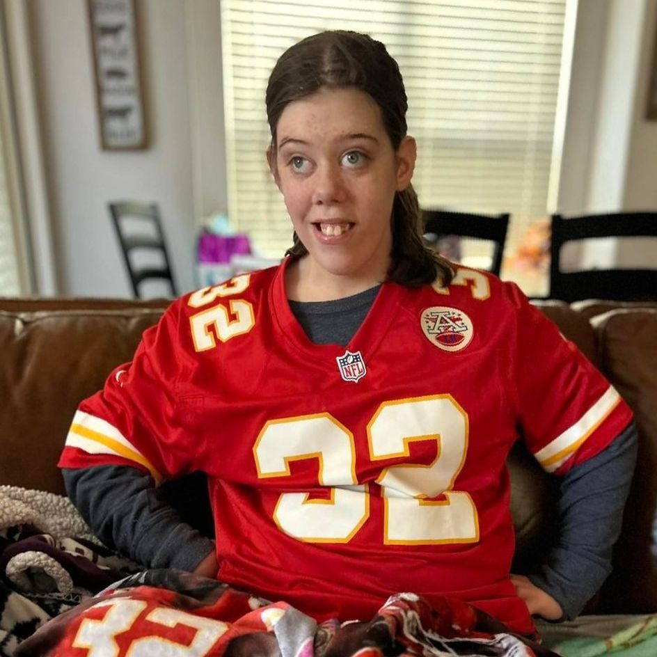 Person wearing a red Kansas City Chiefs jersey with the number 32, seated indoors.