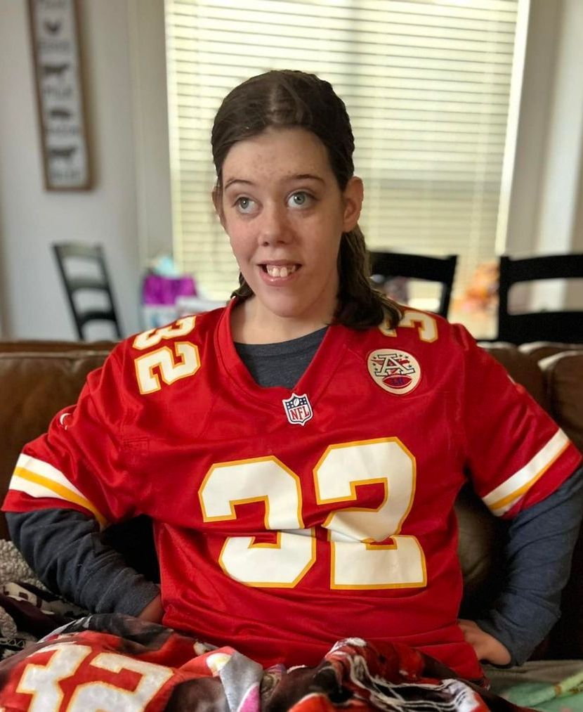 Person wearing a red Kansas City Chiefs jersey, smiling, sitting on a couch.