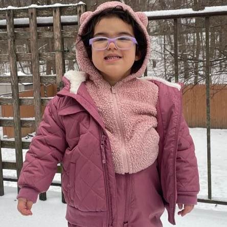 Child in pink winter clothes with eyeglasses in snow.