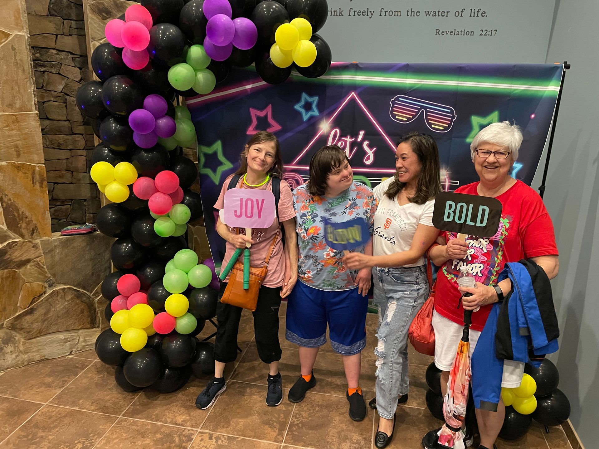 Group of four people posing for photo booth with balloon arch.