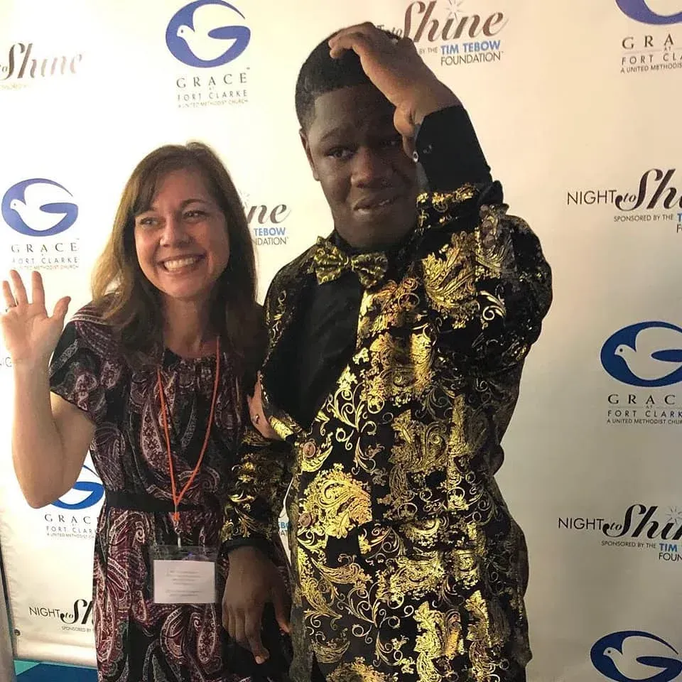 Woman waves next to a man in a gold patterned suit at an event with