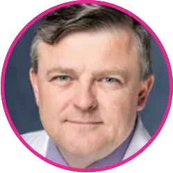 Man in a white coat, blue eyes, inside a pink circle frame.