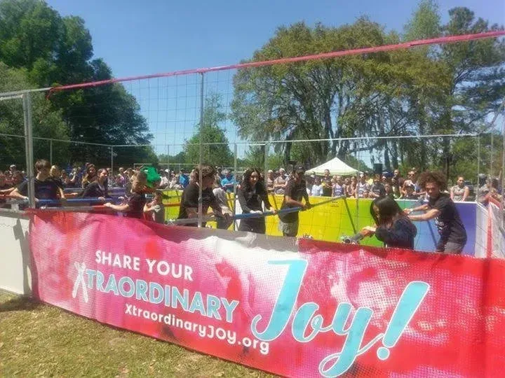People playing in a pit with a net over it, banner reads