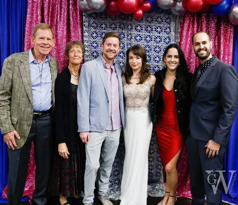 Group of six people posing for a photo against a pink and blue backdrop, smiling.