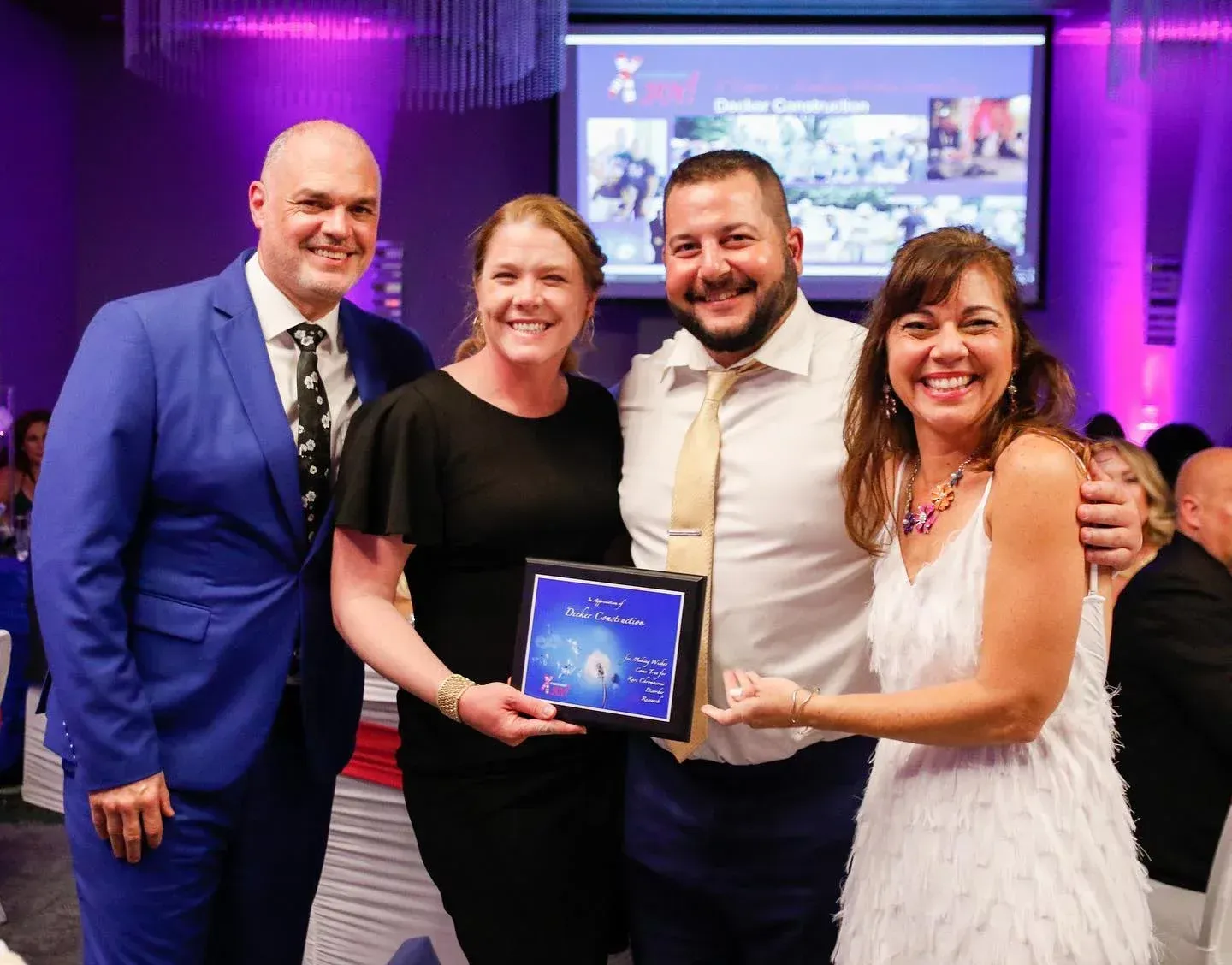 Four people smiling, holding an award, at an event.